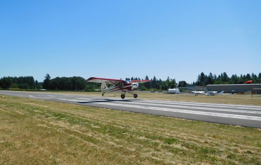 A small tailwheel aircraft landing on Grove Field's runway on a clear day
